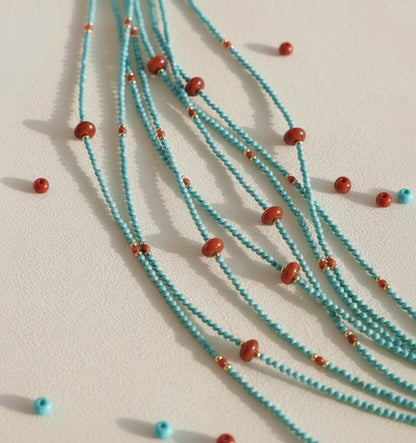 Turquoise beaded necklace with red beads on a light beige background