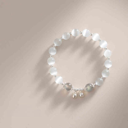 Beaded bracelet with white stones and silver charms on a neutral background